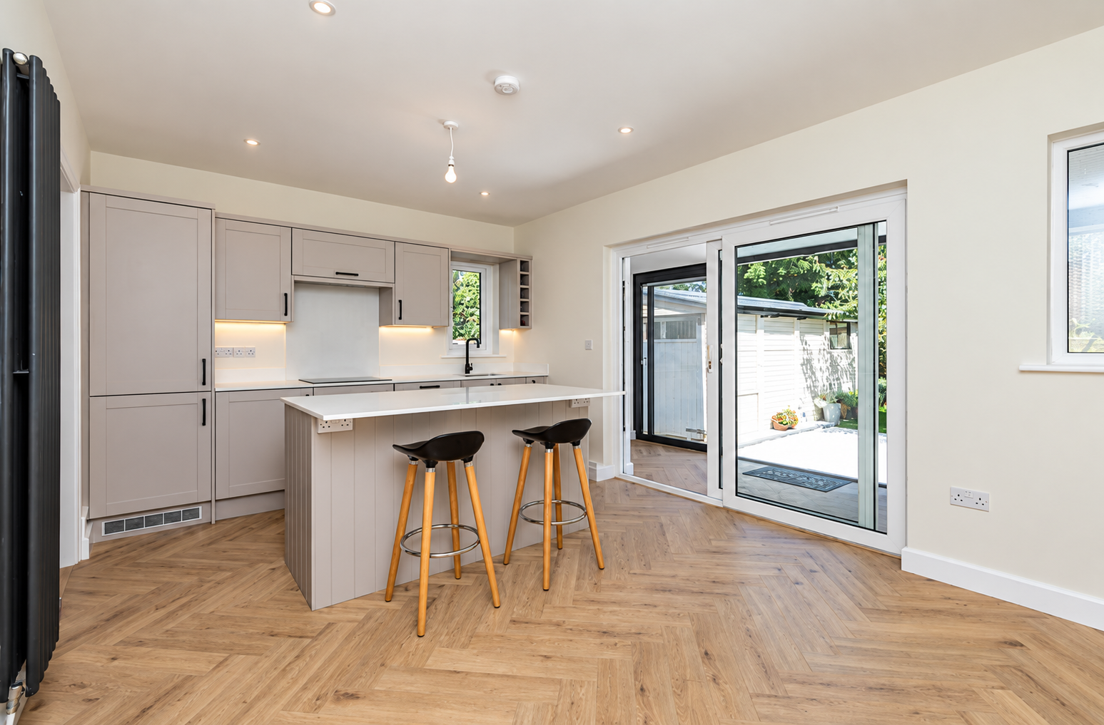 Finished pale kitchen with an island and doors opening to the garden